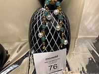 Charm bracelet displayed draped over decorative pineapple stand, showing green agate stones, white pearls, and gold beads.