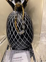 Charm bracelet displayed on a decorative black and white pineapple stand, showing smooth round grey agate stones and gold-tone bead accents along a fine gold chain.