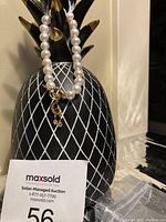 Pearl bracelet displayed on black pineapple-shaped holder with tag showing auction lot number.