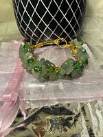 Front angled view of handmade copper wire bangle adorned with green jade, agate, and crystal beads, displayed on a pink organza pouch with a black background.
