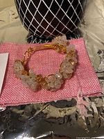 Handmade copper wire bangle with clustered light pink love quartz and crystal beads displayed on a black and white patterned holder on a pink fabric pouch, shown from above and side angles.