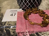 Copper wire bangle handmade with tiger eye chips and small clear and amber crystal beads, placed on a pink fabric pouch next to a black and white patterned vase.