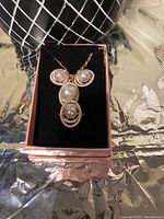 Front view of the pearl pendant and necklace displayed in a pink box with black velvet interior.