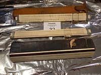 Three vintage Keuffel & Esser slide rulers, two with worn tan leather cases and one without a case, laid out horizontally.