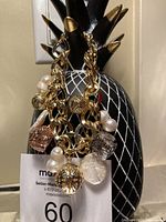 Photo of tricolour charm bracelet with appetizer pineapple display in background, charms visible in gold, silver, and rose gold tones with pearls.