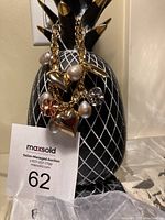 Front view of tricolour charm bracelet hanging on a black and gold pineapple display stand, showing pearls and heart-shaped charms.