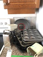 Overview of metal muffin tins, loaf pans and cooling racks arranged on kitchen counter and stove top.