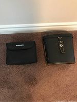 Two closed cases side by side on carpet: a black soft Bushnell case and a black leather Kalimar case with snap latch.