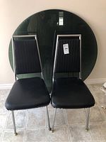 Front view of two black retro vinyl chairs placed side by side showing vertical stitching on backrests, chrome legs, and vinyl seats.