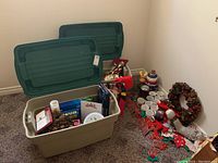 Two large plastic storage bins filled with Christmas decorations and items set on floor against wall.