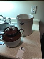 Both items on countertop: the white ceramic crock with blue logo marked No 1 and the brown-beige covered bean pot with lid beside it.