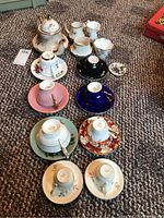 Overview of nine cups and saucers along with ceramic teapot, creamer, and sugar bowl on carpet
