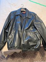 Front view of the Danier black leather bomber jacket laid flat showing zipper front, pockets, and collar.