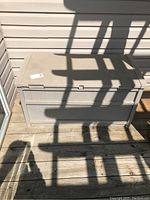 Beige Suncast plastic deck box closed, showing size and shape on wooden deck.