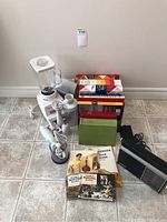 Full view of the kitchen lot showing Osterizer blender, Braun immersion blender attachments, various cookbooks, and other kitchen items on a tiled floor against a wall.