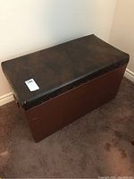 Front and top view of the rectangular wooden storage box with dark brown faux leather padded seat showing metal studs detail and flat wooden sides.