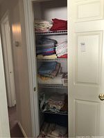 Closet with multiple shelves filled with folded linens including bedding and towels in various colors.