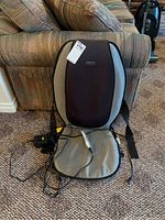 Full front view of Homedics power massage seat cover resting against couch with cords and control remote visible.