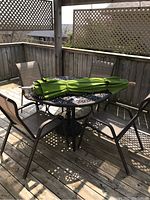 Photo of patio table with four chairs and folded green umbrella on deck showing overall set and condition.