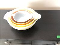 Stacked set of 4 nesting Pyrex bowls in graduated sizes and colors on dark tabletop