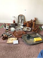 Full view of all serving and decor pieces arranged on carpet including wooden bowls, metal trays, glass bowl with lid, wooden bunny figure, salt and pepper grinders, and various small items.