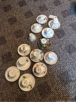 Photo of 12 teacups and saucers plus one extra cup laid out on carpet, showing varied designs and patterns.