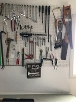 Wide view of pegboard with an assortment of hand tools hanging including wrenches, pliers, screwdrivers, hammers, and saws.