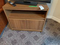 Front view of wooden TV stand showing top surface, open middle shelf, and closed two-door cabinet below.
