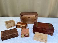 Overview of six decorative boxes on white cloth, showing variety in size, color, and material including carved wood and carved stone