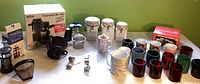 Overview photo of all items including Braun espresso maker boxed, French press with box, ceramic lidded containers, coffee filter accessories, floral and plain mugs, and metallic colored mugs