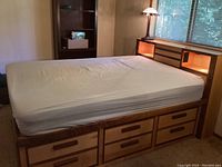 Full view of the full size bed frame showing white covered mattress, six drawers on one side and headboard with lighted open shelves.