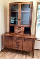 Front view of the entire two-piece wooden hutch cabinet showing glass-paneled doors on the upper portion and multiple drawers and cabinets on lower portion.
