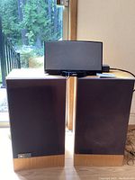 Pair of JBL speakers with wood finish and fabric grills, positioned near a window, cables visible on the floor