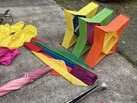 Colorful box kites and pink striped umbrella on pavement.