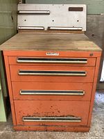 Front view of orange metal tool cabinet showing four drawers with metal handles labeled 'Equipto' and 'Sobieck', wood top surface, visible rust and paint wear on bottom drawer