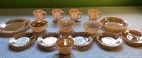 Front view of full set of peach Fire King lusterware dishes on table, including mugs, bowls, plates, and saucers arranged in rows.