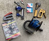 Lot layout on carpet showing pneumatic nailer, staplers, coiled hose, hammer, and staple boxes.
