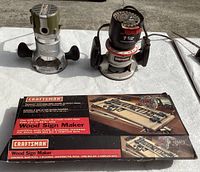Two corded fixed base routers side by side and the boxed Wood Sign Maker kit on a white surface.
