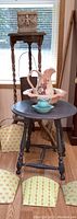 Overall view of small round blue shabby chic table with vintage pitchers and basins, taller wooden plant stand, baskets or tins on floor