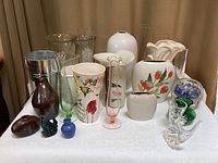 Front view of all pottery, glass, and metal vases along with floral arranging items placed on a white surface