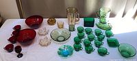 Wide shot of the entire vibrant vintage glass collection arranged on a table in natural light showing red, green, clear, and amber colored glass items.