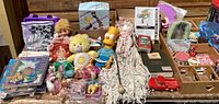 Overview of the vintage toys lot showing dolls, Care Bear, Bart Simpson figure, pony figurines, roller skates box and assorted puzzles and toys displayed on wooden surface.