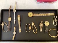 Overview of all eleven vintage women's wristwatches arranged on a tray showing various bands and face shapes.