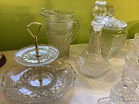 Photo showing a two-tier glass serving stand with intricate patterning, a decanter with stopper, and a lidded jar in patterned Wexford cut glass.