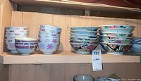 Long view of shelf with stacked Asian bowls in various designs and sizes, some featuring birds and floral patterns, others geometric motifs in purple.