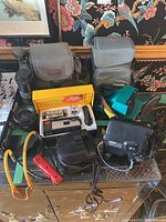 Overview showing multiple items including two camera bags, assorted cameras, lenses, binoculars, and accessories.