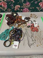 Overview photo of entire collection of costume jewelry laid out on a flat surface including necklaces, bracelets, earrings, and watches of various colors and styles.
