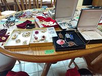 Full view of assorted costume jewelry spread on table including brooches, necklaces, and earrings in boxes and loose on surface.