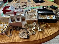 Full view of assorted costume jewelry on wooden table including boxed and loose pieces such as necklaces, brooches and earrings.