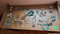 Overview of costume jewelry lot spread on a wooden surface including earrings, bracelets, chains, and a metal pin.
